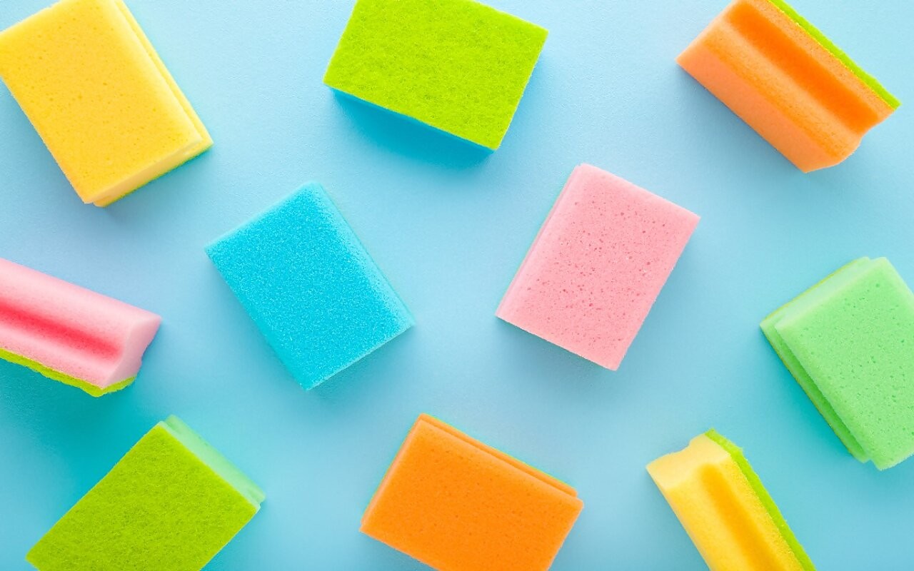 New colorful dry sponges on light blue table background. Pastel color. Closeup. Pattern of cleaning products. Top down view.
